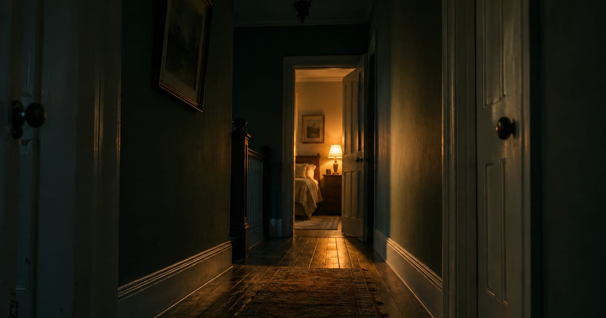A dark hallway at night with a single lit doorway at the far end
